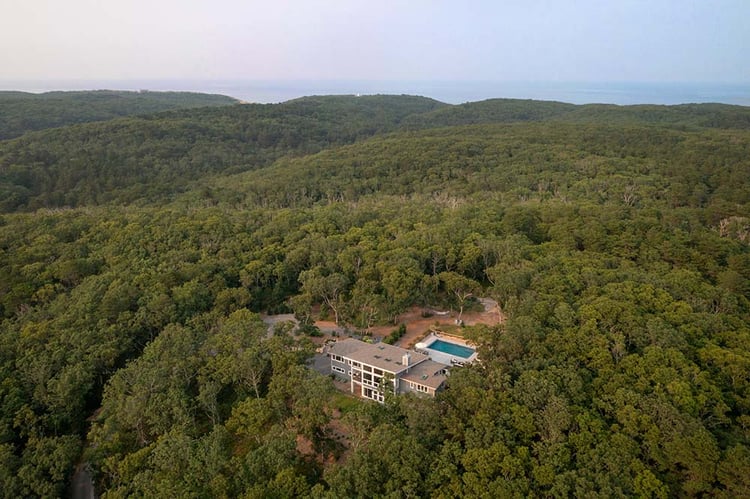 Truro Treehouse by Acorn Deck House Company is a modern farmhouse on Cape Cod. This photo shows an aerial view of the house. The house is surrounded by acres of forest with views of Cape Cod National Seashore in the distance.